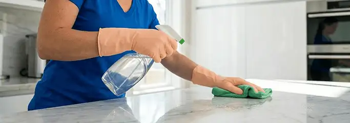 Maid service worker spraying and wiping a kitchen countertop with a microfiber cloth for sanitizing, Fort Wayne, IN.
