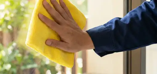 House cleaner wiping a glass window with a yellow microfiber cloth for streak-free cleaning, Fort Wayne, IN.
